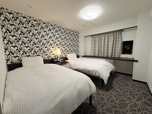 Habitación de hotel con dos camas, un escritorio con computadora, un espejo y una alfombra estampada.