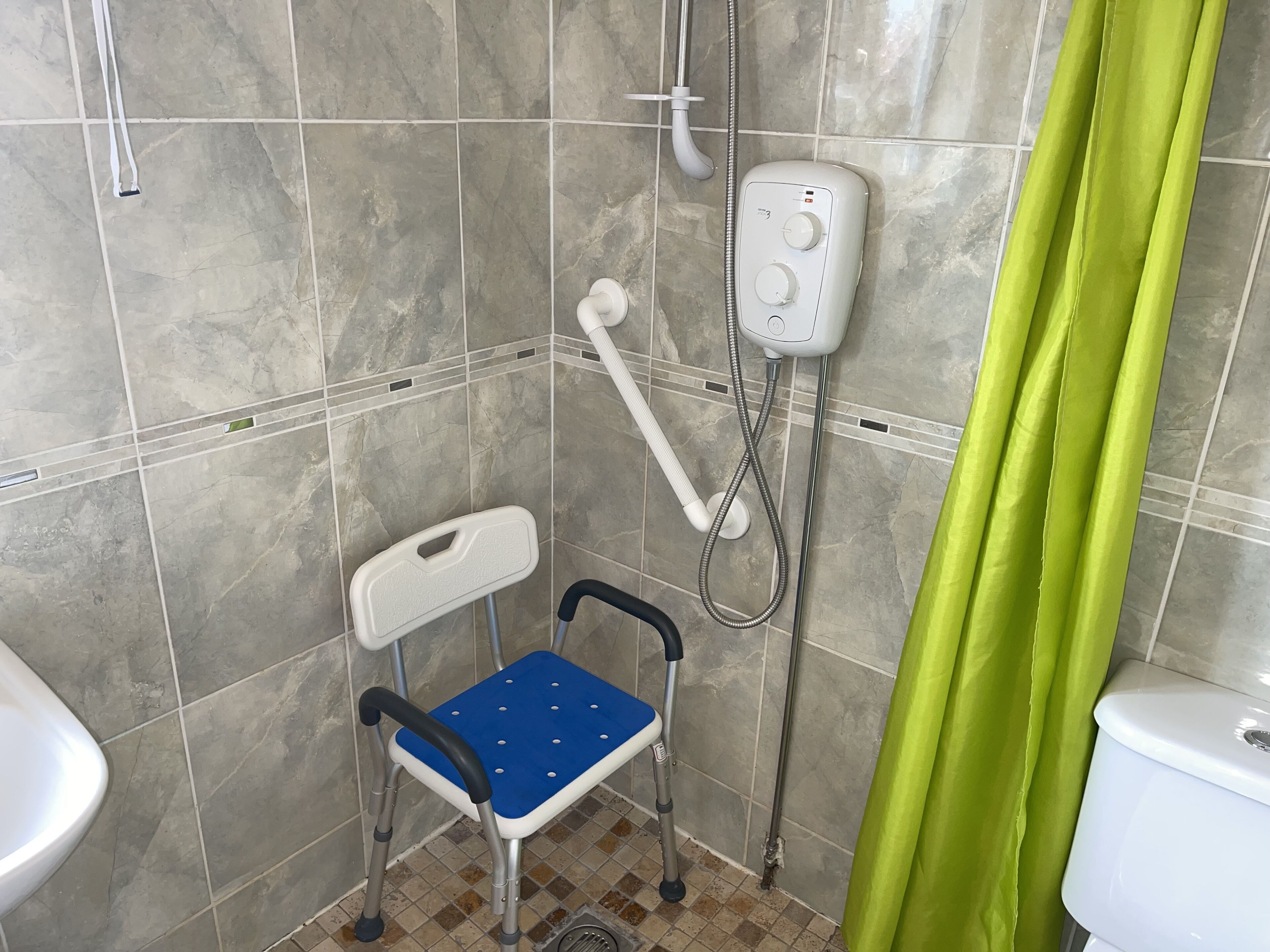 Ein Badezimmer mit Dusche, Toilette und einem rollstuhlgerechten Sitz.