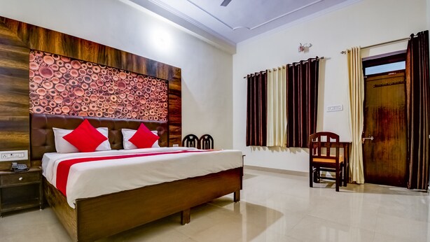 A hotel room with a wooden bed, red pillows, a nightstand, and a wall-mounted decorative panel. - Hotel saif ranthambhore (Sawai Madhopur)
