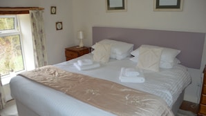 A neatly made bed with white linens and a beige throw blanket, a bedside table with a lamp, and a window with curtains. - The Old Farmhouse
3 bed cottage Hot Tub, Dog/cat friendly  onsite fishing (Pickering)