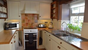 A kitchen with white cabinets, a stainless steel sink, a microwave, a stove, and a window with a view of greenery. - The Old Farmhouse
3 bed cottage Hot Tub, Dog/cat friendly  onsite fishing (Pickering)