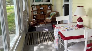 Una habitación con una mesa, sillas, un ventilador de techo, una estantería y una ventana.