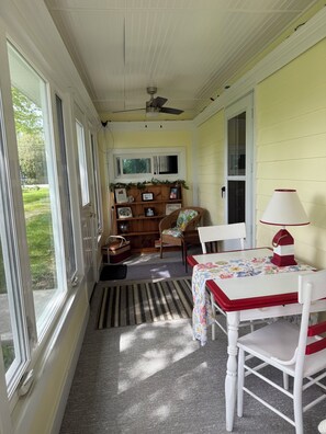 A room with a table and chairs, a ceiling fan, a bookshelf, and a window.