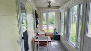 Un porche techado con una mesa y sillas de comedor, un ventilador de techo y vista al jardín trasero.