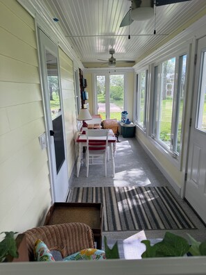 A covered porch with a dining table and chairs, a ceiling fan, and a view of the backyard.
