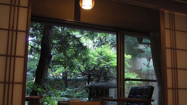 Una habitación japonesa tradicional con suelo de tatami, una mesa baja y vistas a un jardín exuberante a través de grandes puertas correderas.