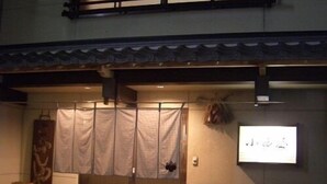 Una entrada japonesa tradicional con puerta corredera, una estructura similar a un santuario y un letrero colgado en la pared.