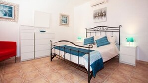 Een slaapkamer met een metalen bedframe, een witte nachtkastje, een rode stoel en een witte kledingkast.