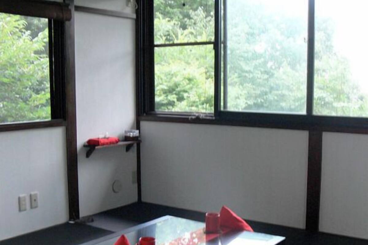A room with tatami flooring, a low table with a cushion, and a view of greenery through large windows.