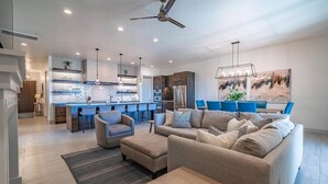 A modern living room with a sofa, armchair, and coffee table. There is a kitchen area with a bar and seating. - Arcadia 37 | Fire Pit * Luxury Vacation Villa * Sleeps 18 * Balcony Views (Santa Clara)