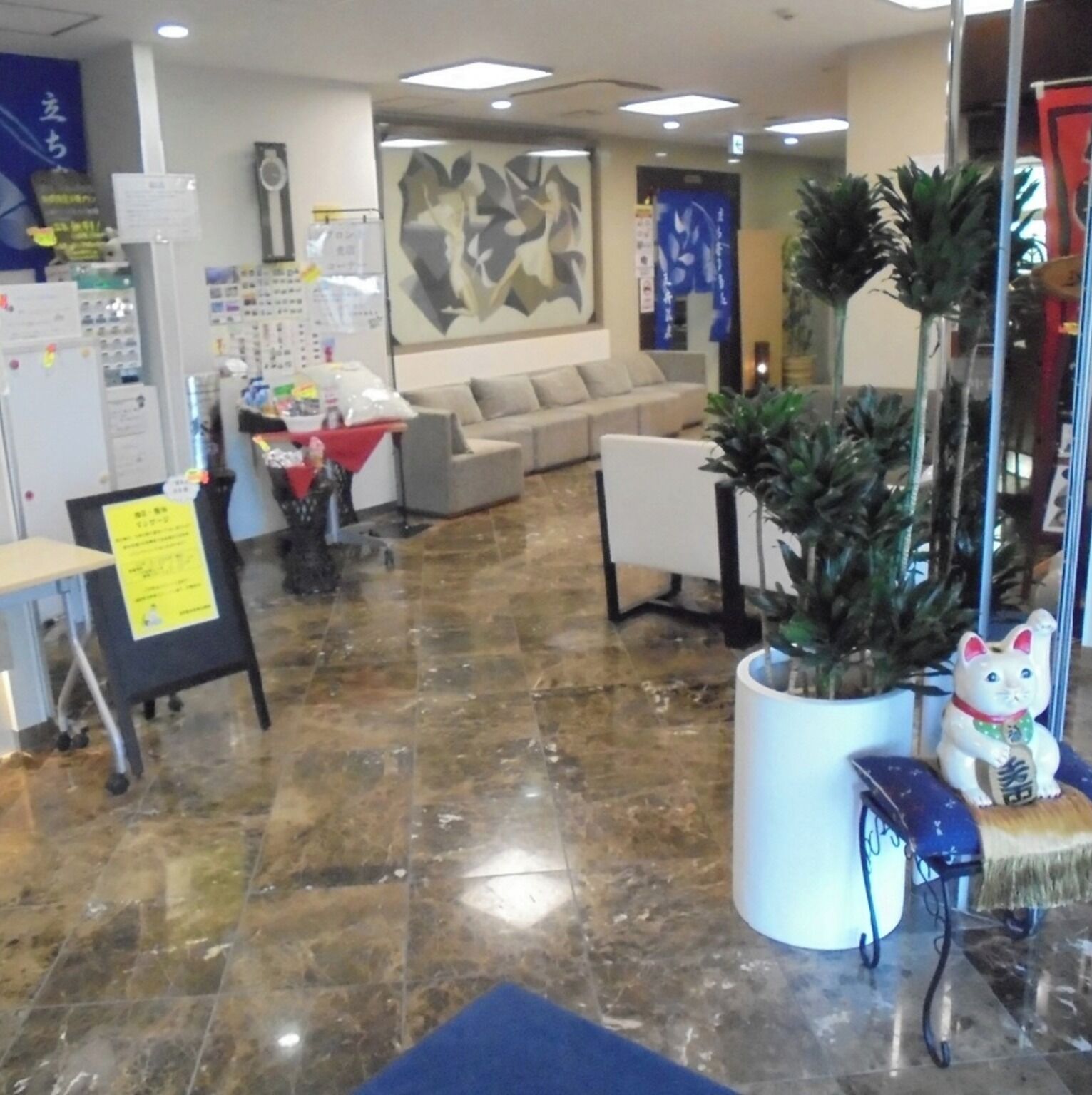 Un hall con mostrador de recepción, un sofá, una mesa de centro y una planta en maceta.