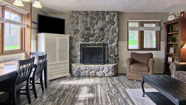 A living room with a stone fireplace, a dining area with a table and chairs, and a cozy seating area with a chair and a sofa.