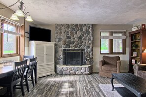 A living room with a stone fireplace, a dining area with a table and chairs, and a cozy seating area with a chair and a sofa.