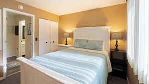 A bedroom with a bed, two bedside tables, a nightstand, a door, and a hallway.