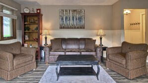 A living room with a brown leather sofa, two armchairs, a coffee table, a clock, a fireplace, and a painting on the wall.