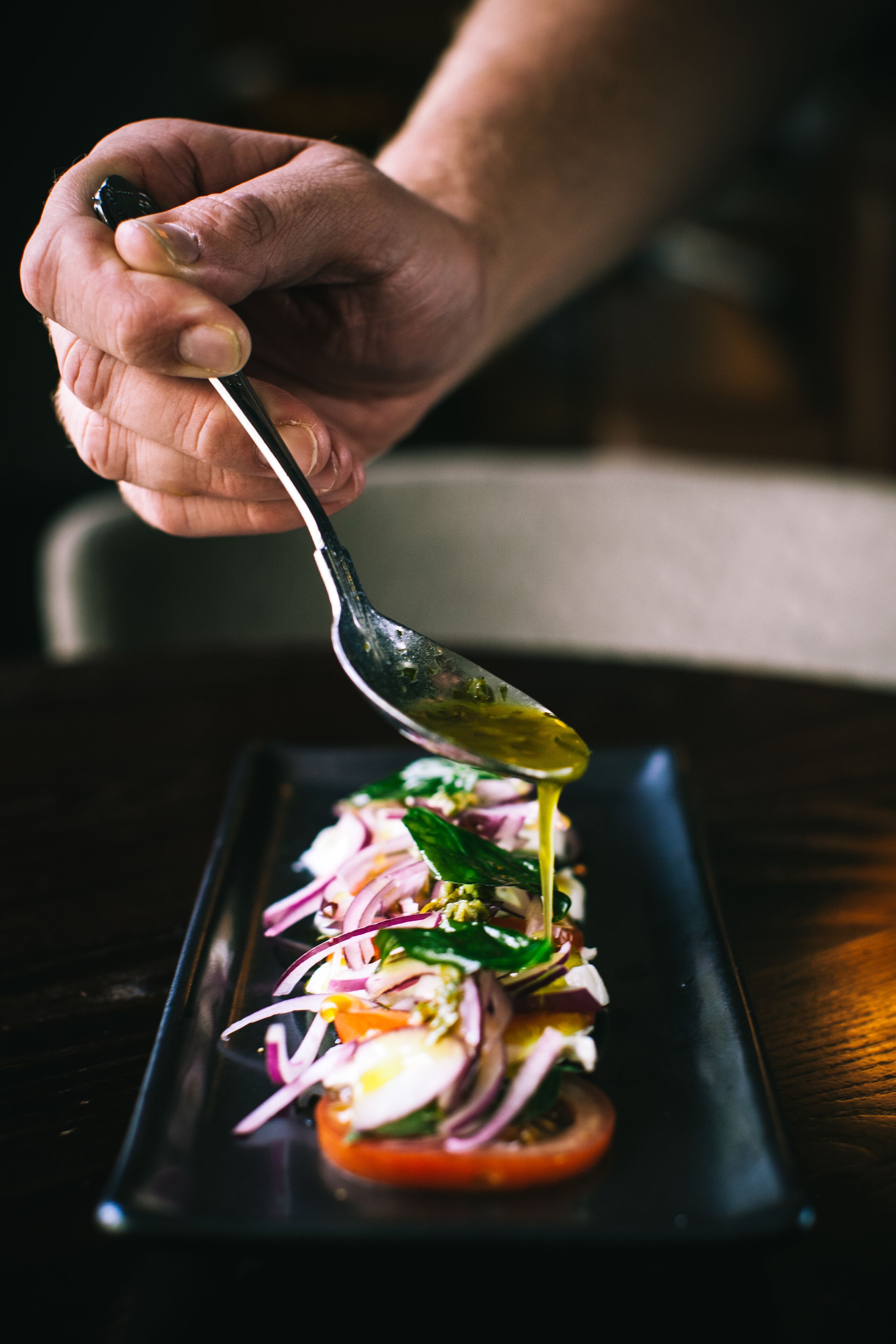 A hand pouring dressing over a salad on a rectangular plate.