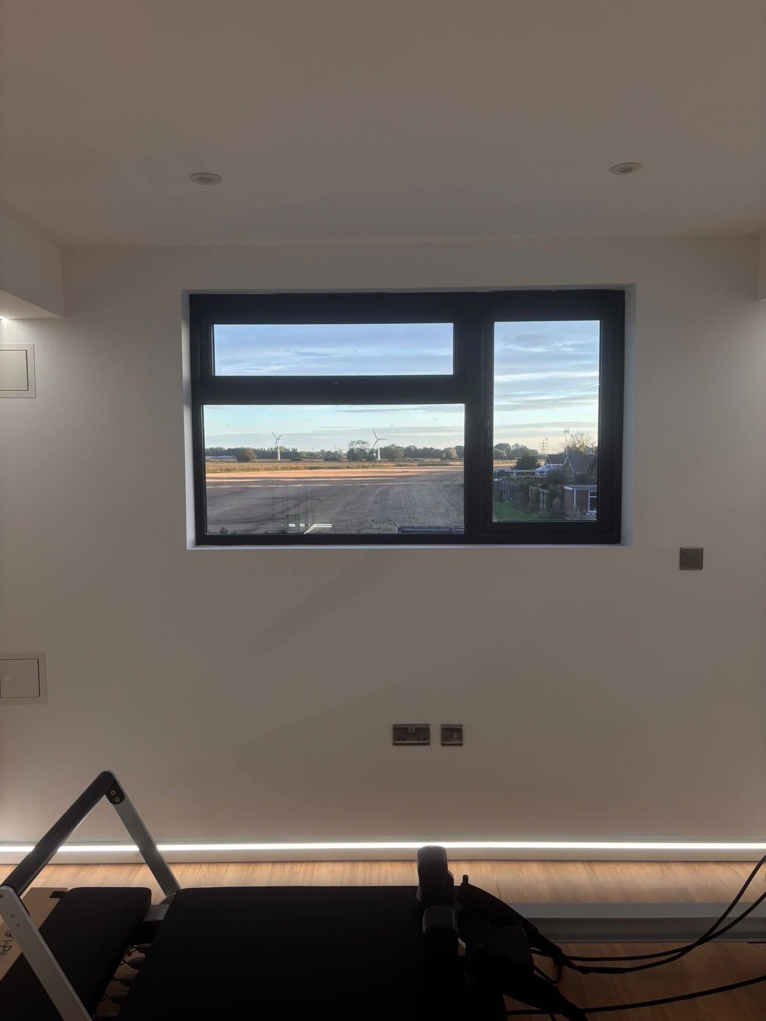 A room with a large window, a treadmill, and a wall-mounted light fixture.