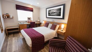 A hotel room with a bed, bedside tables, a desk, a chair, and a large framed picture on the wall.