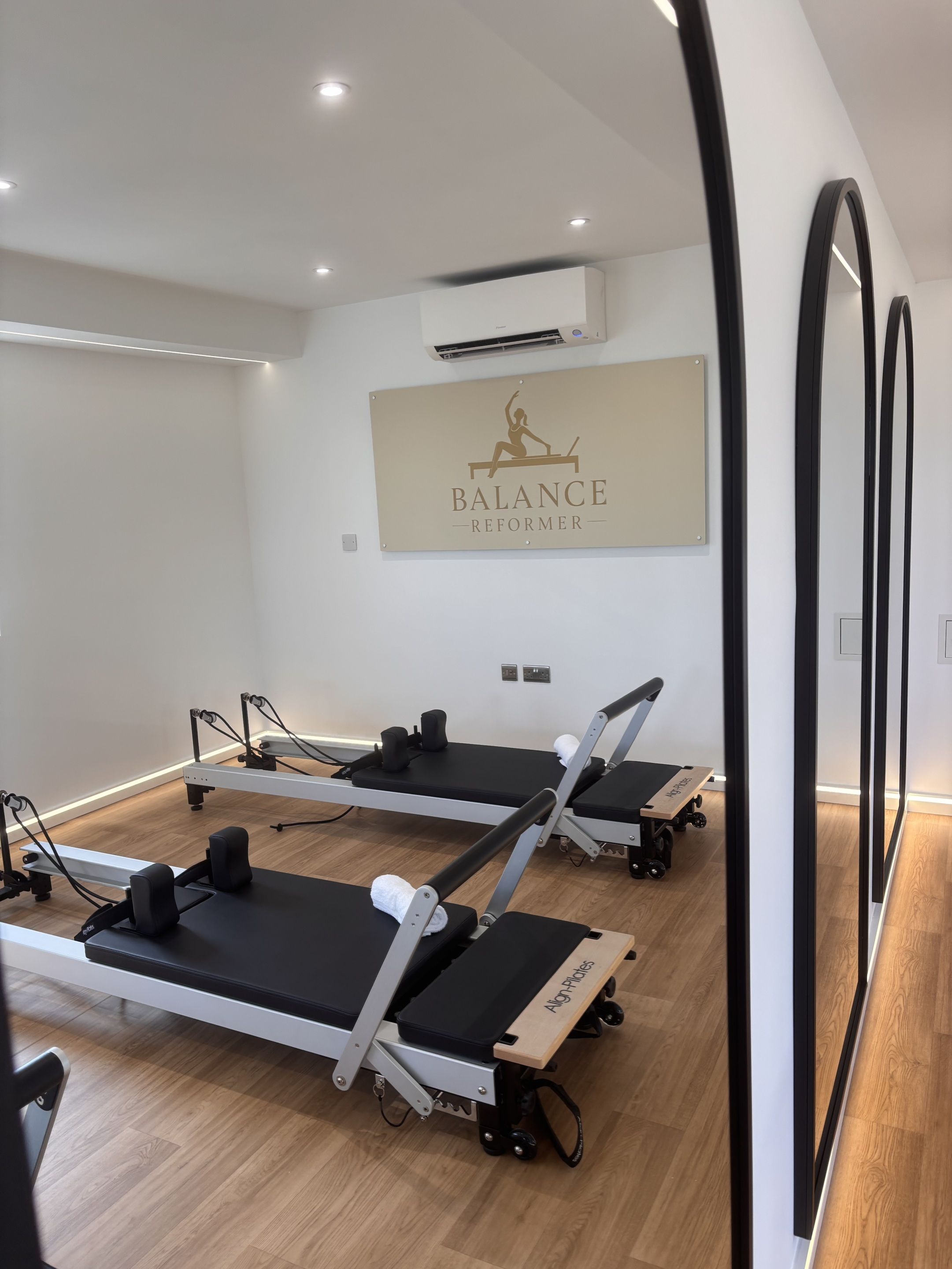 Una stanza con tre macchinari Pilates Reformer, un condizionatore d'aria a parete e un cartello con scritto 'BALANCE REFORMER'.