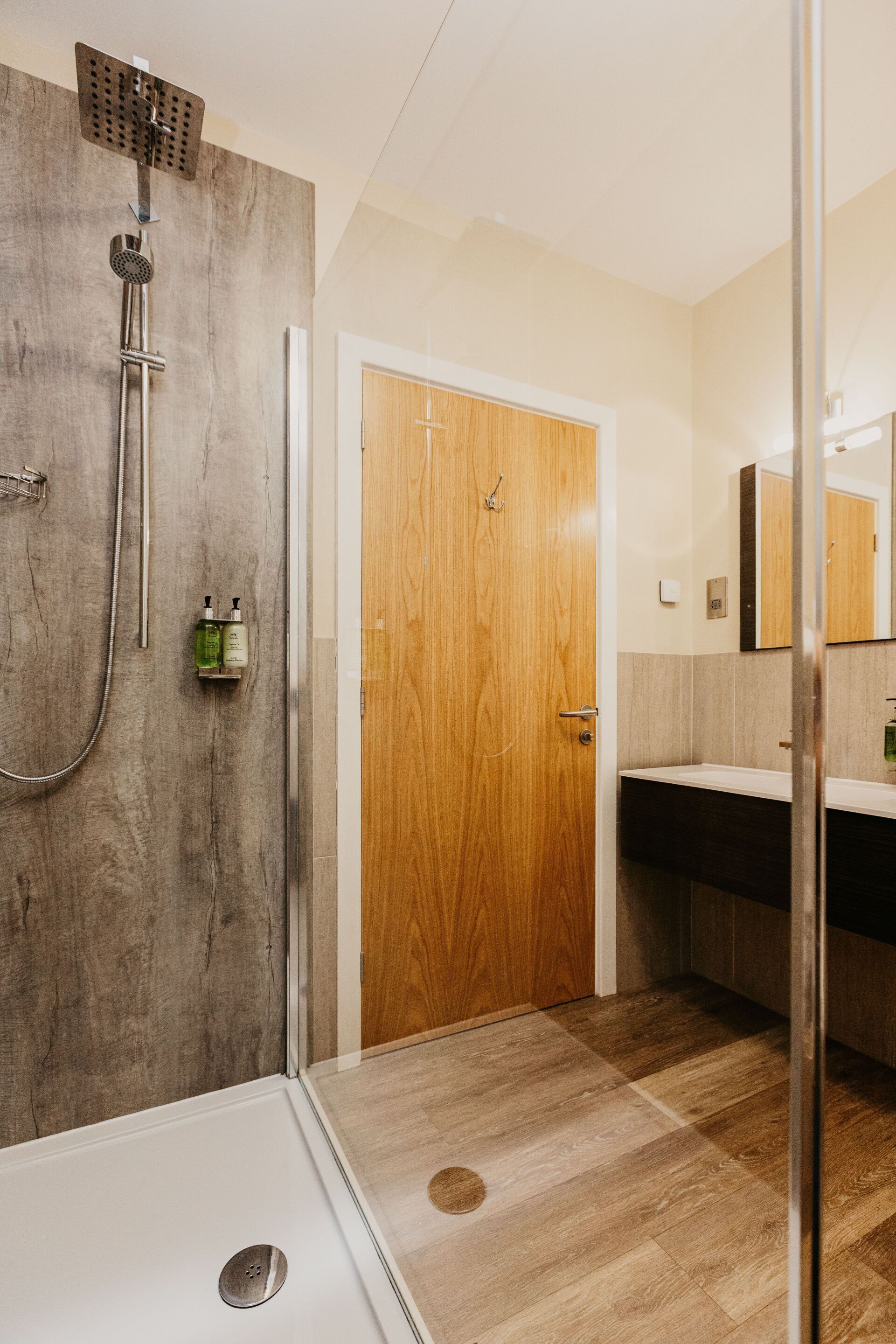 A modern bathroom with a shower, a wooden door, a sink, and a mirror.