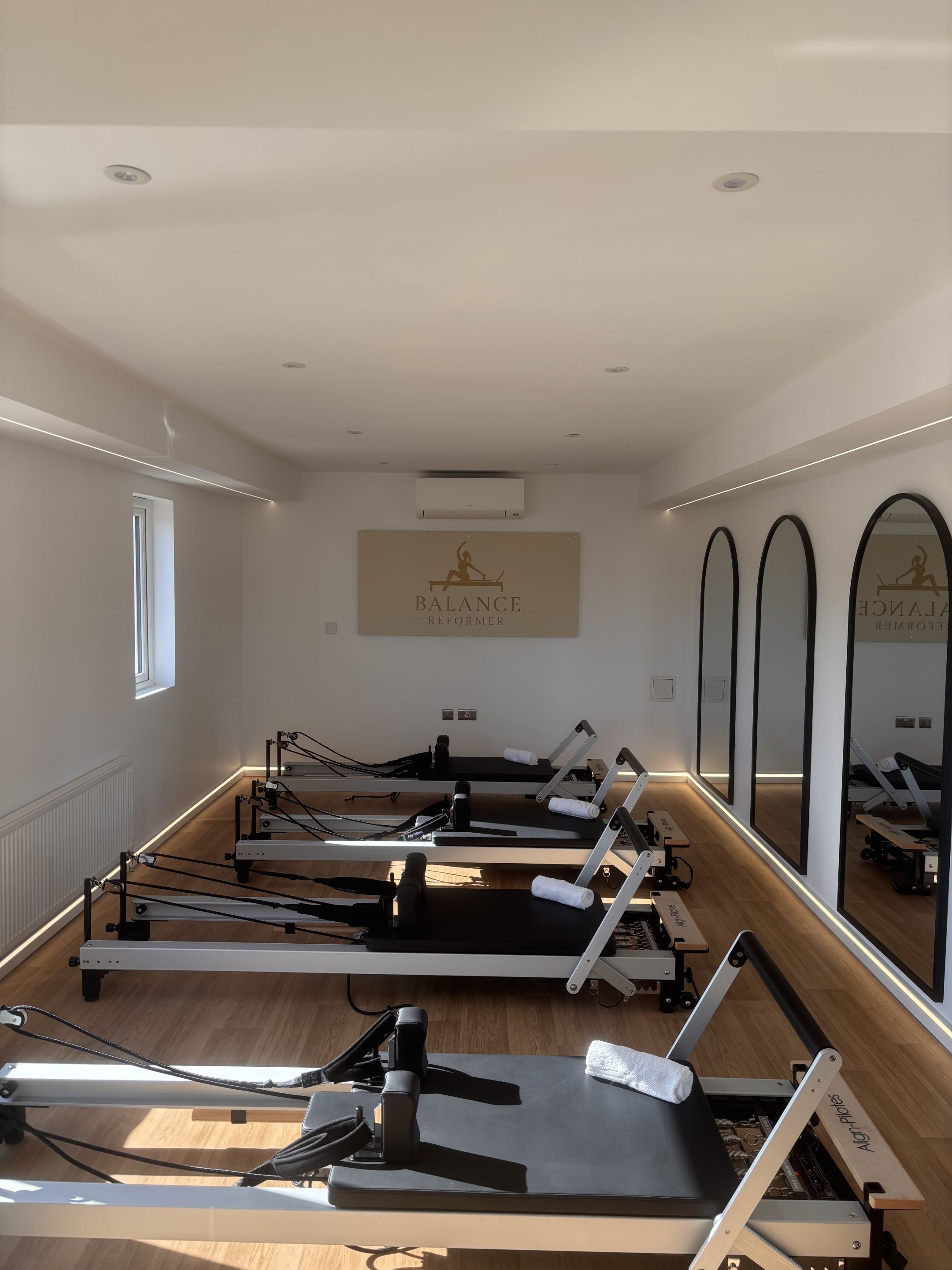 A Pilates studio with equipment, a wall-mounted logo, and mirrors.