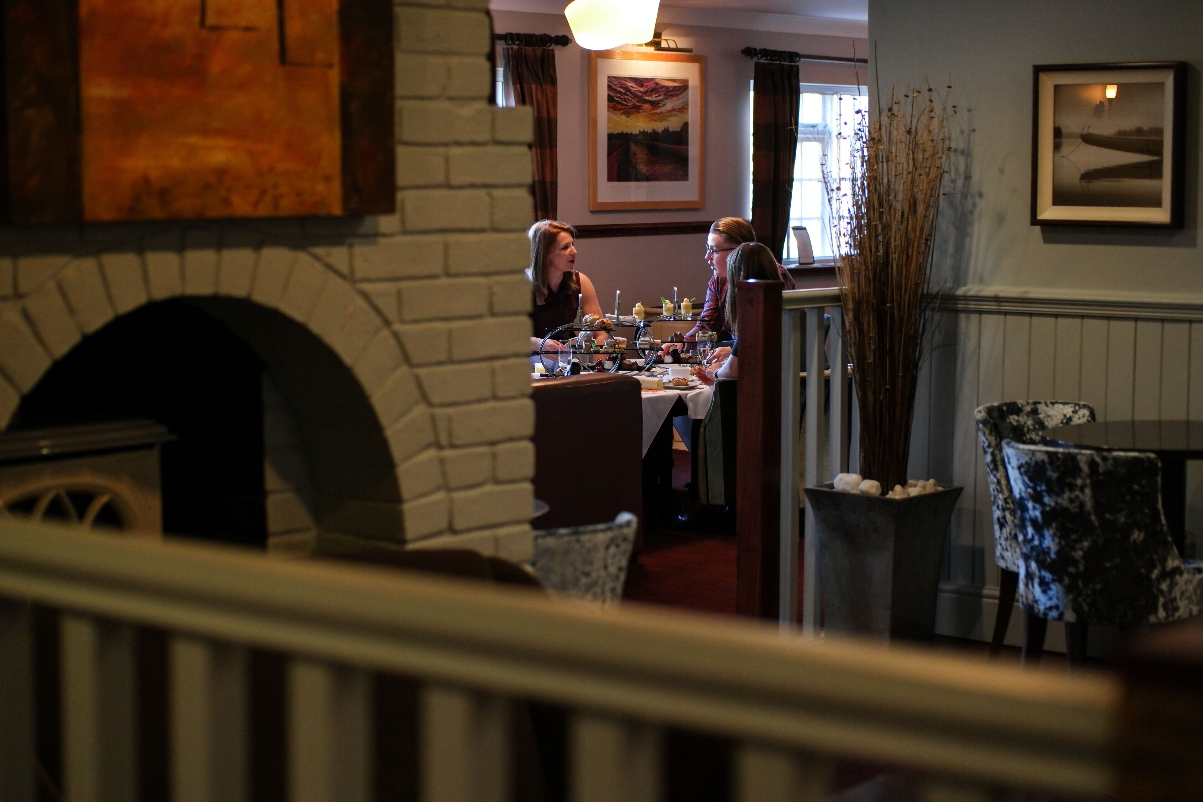 A restaurant with a brick fireplace, dining tables, and chairs. There are framed pictures on the walls.