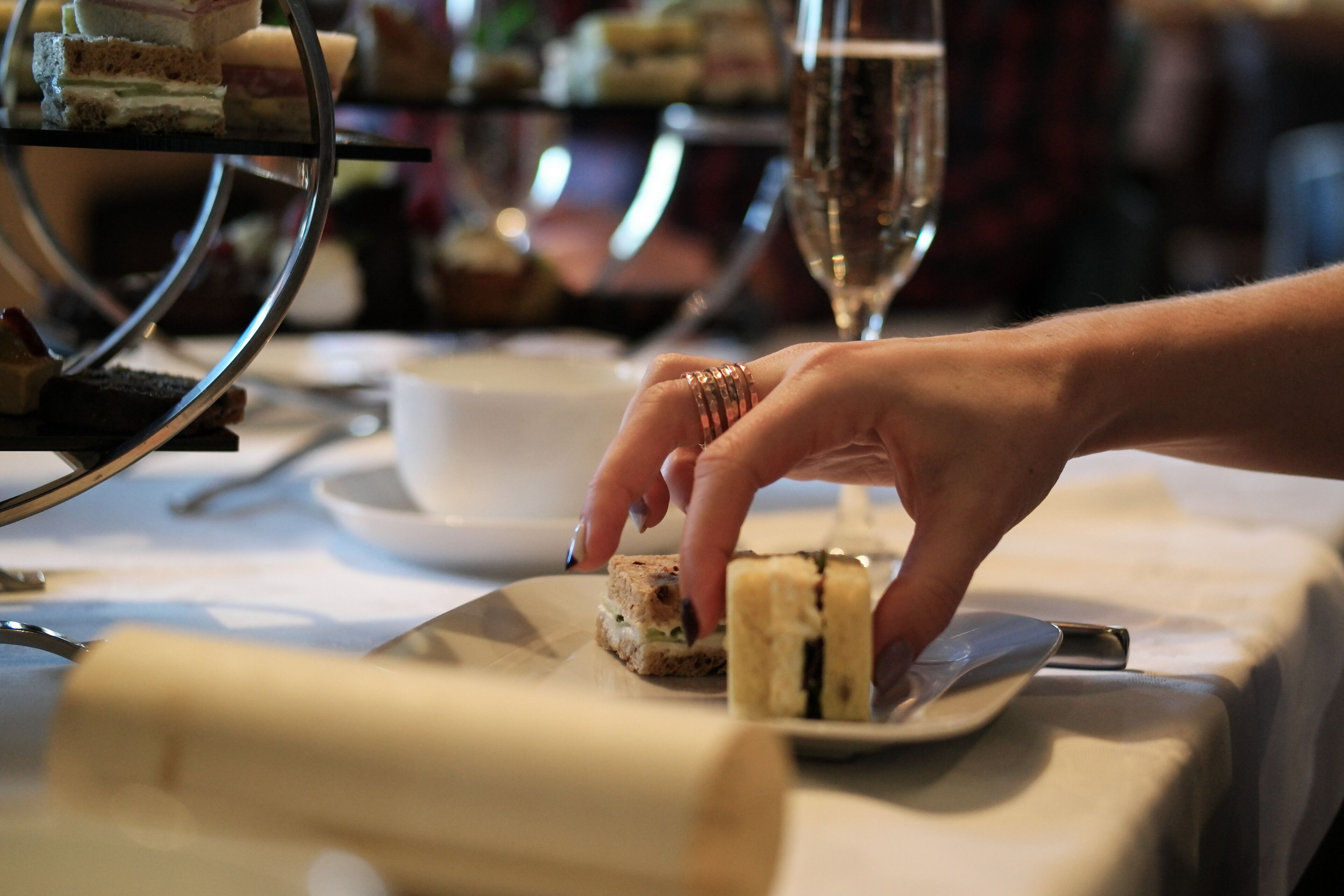 A hand placing a sandwich on a plate at a table with a glass of water and a cup.