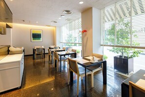 A modern restaurant with a clean, minimalist interior, featuring a mix of wooden and metal furniture, a large window with blinds, and a contemporary art piece on the wall. - Four Season Tokushima (Tokushima)