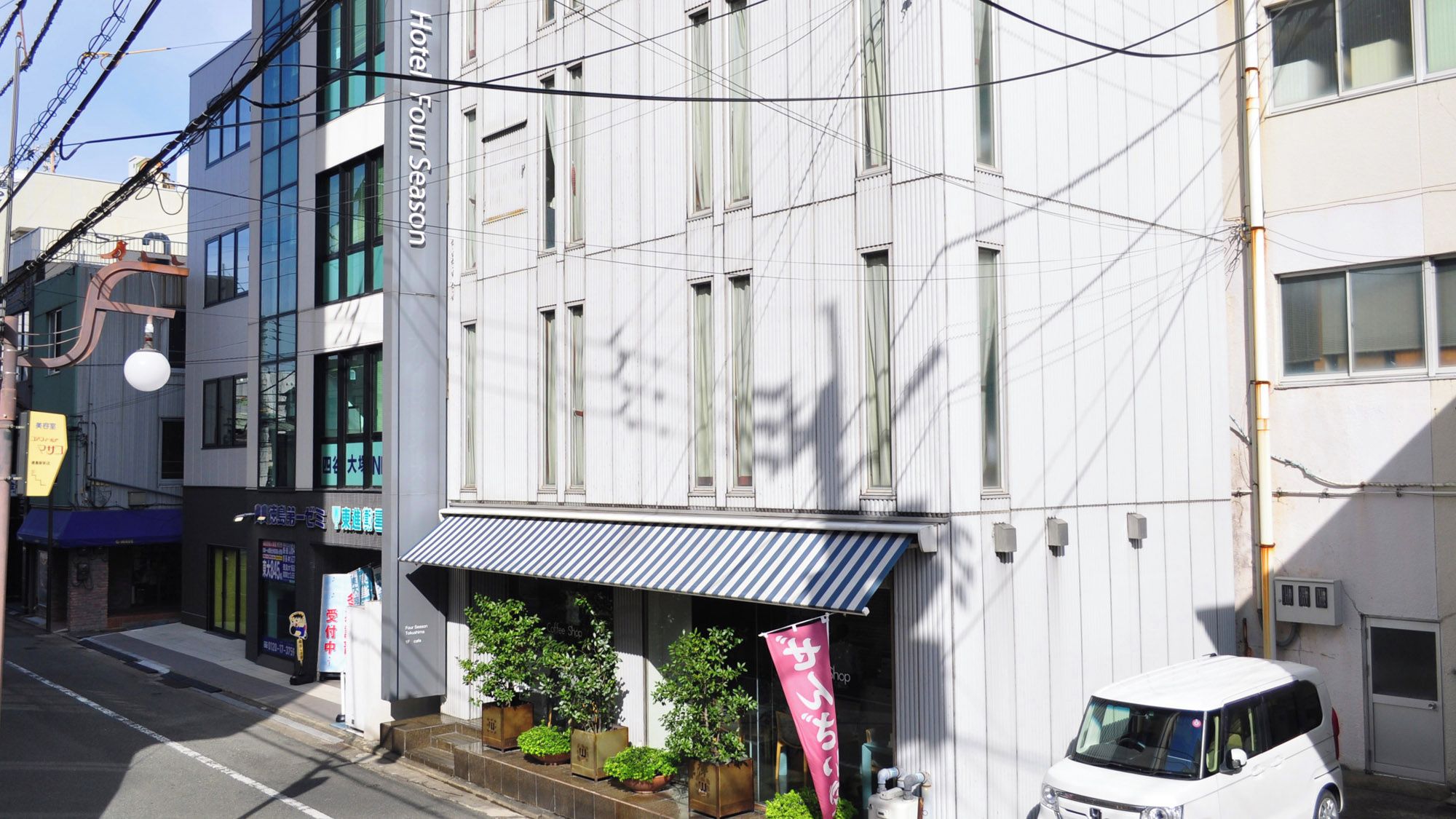 A hotel with a sign reading 'Hotel Four Season' and a storefront with a striped awning.