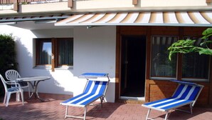 Eine Terrasse mit zwei gestreiften Liegestühlen, einem kleinen Tisch und einem weißen Stuhl.