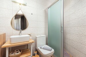 A bathroom with a white sink, a mirror, a toilet, and a shower area.