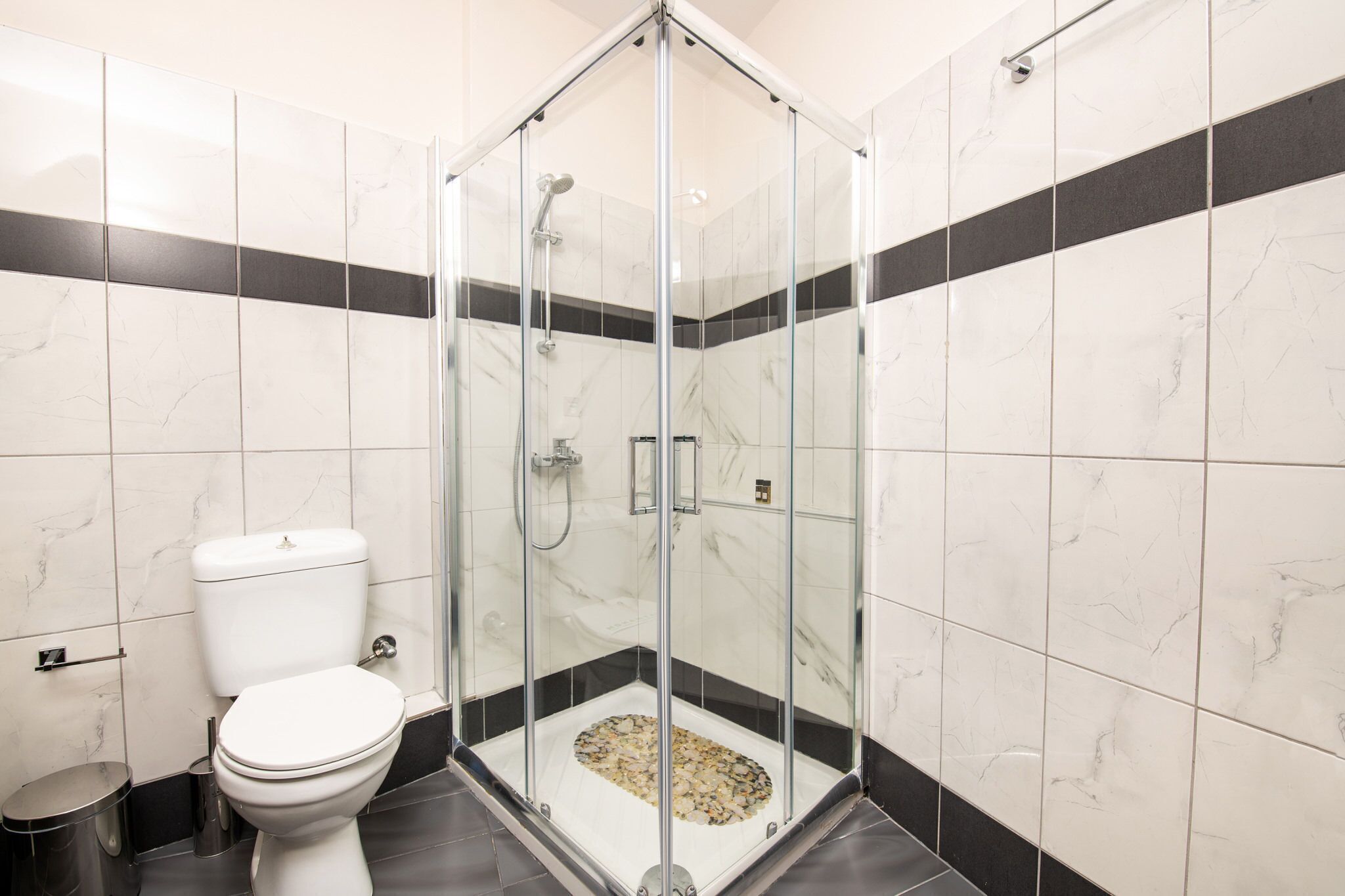A modern bathroom with a glass-enclosed shower, a toilet, and a trash bin.