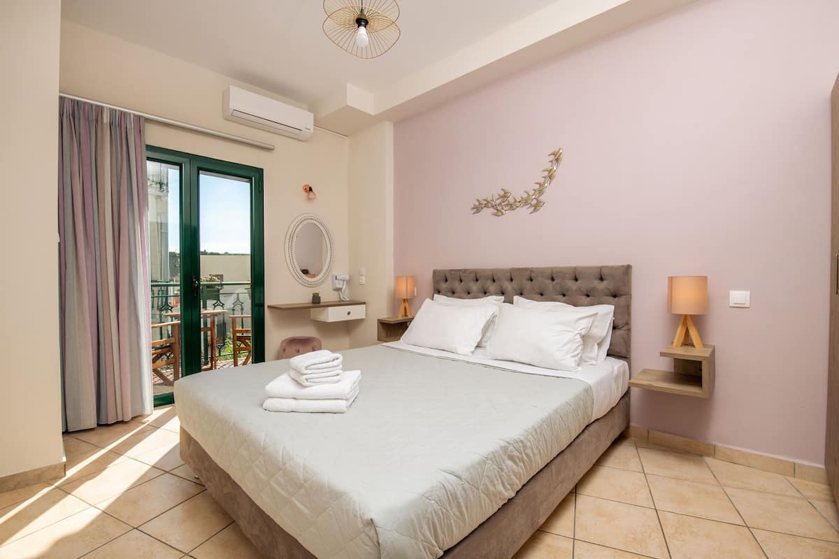 Un lit bien fait, avec du linge de lit blanc et une serviette pliée posée sur le côté, une table de chevet avec une lampe, un miroir fixé au mur et une vue sur l’extérieur, accessible par une porte coulissante.