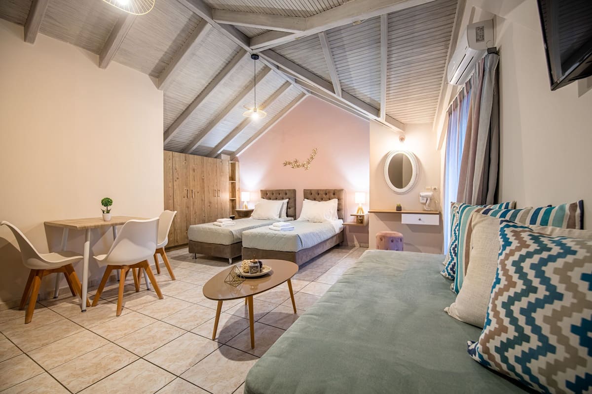 Une pièce confortable avec un plafond haut, un lit, un canapé, une table à manger avec des chaises et une petite table agrémentée d’un objet décoratif.