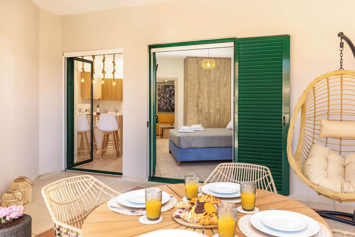 Un coin repas avec une table dressée pour deux personnes, une chaise en osier et un fauteuil suspendu.
