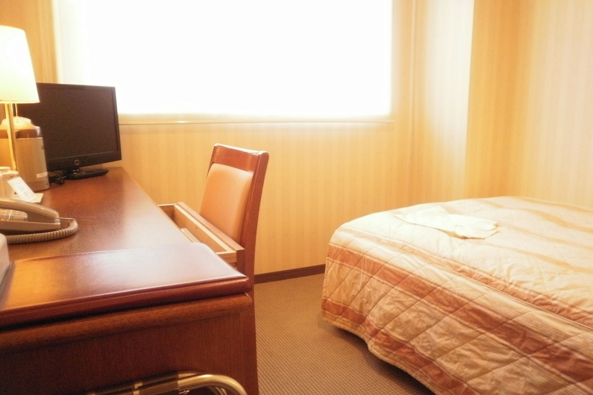 A hotel room with a bed, a desk with a telephone, a lamp, and a television.