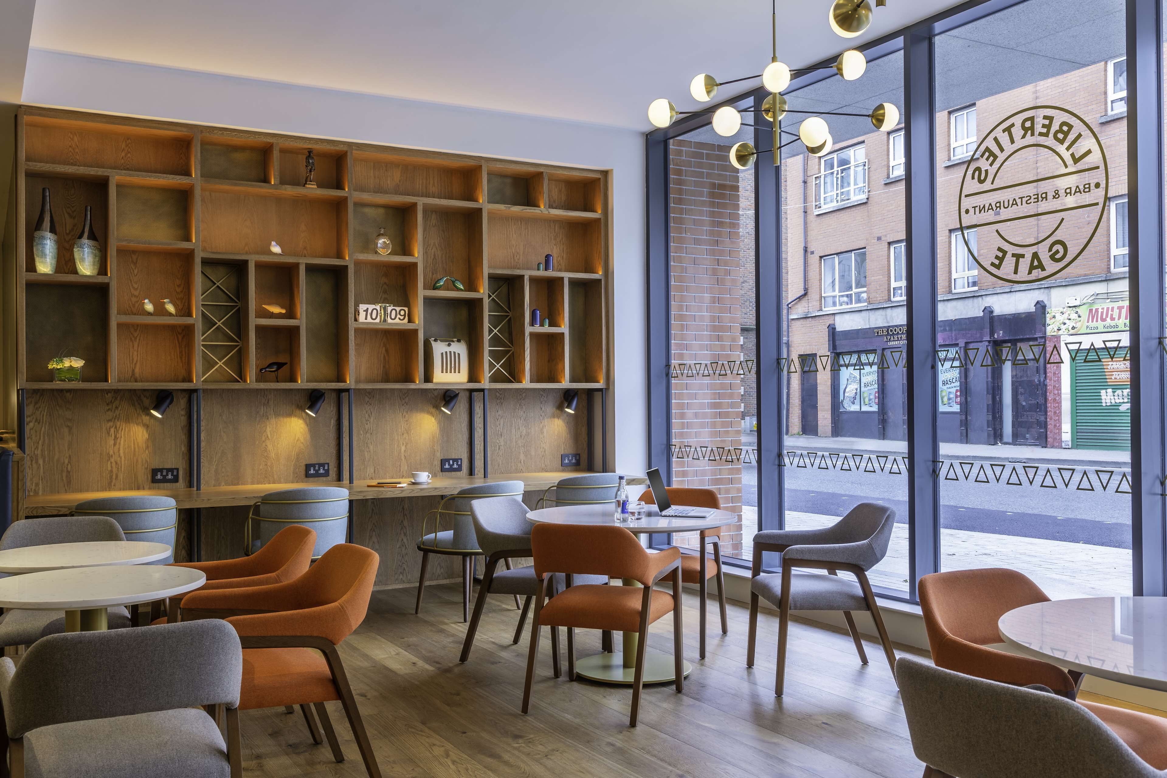 A modern cafe with wooden shelves, round tables, and orange chairs.