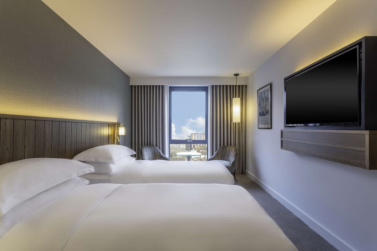 Een hotelkamer met twee bedden, een groot raam, een flatscreen televisie en uitzicht op de stad.