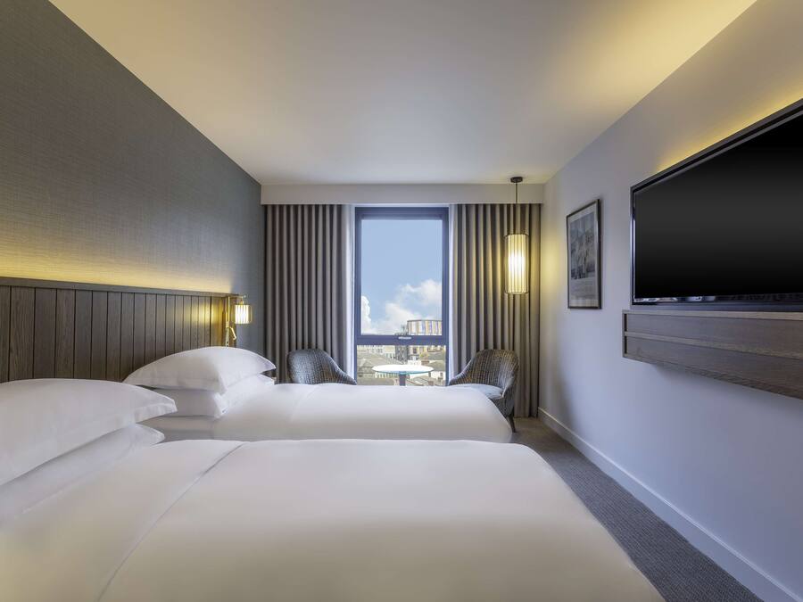 Een hotelkamer met twee bedden, een groot raam, een flatscreen televisie en uitzicht op de stad.