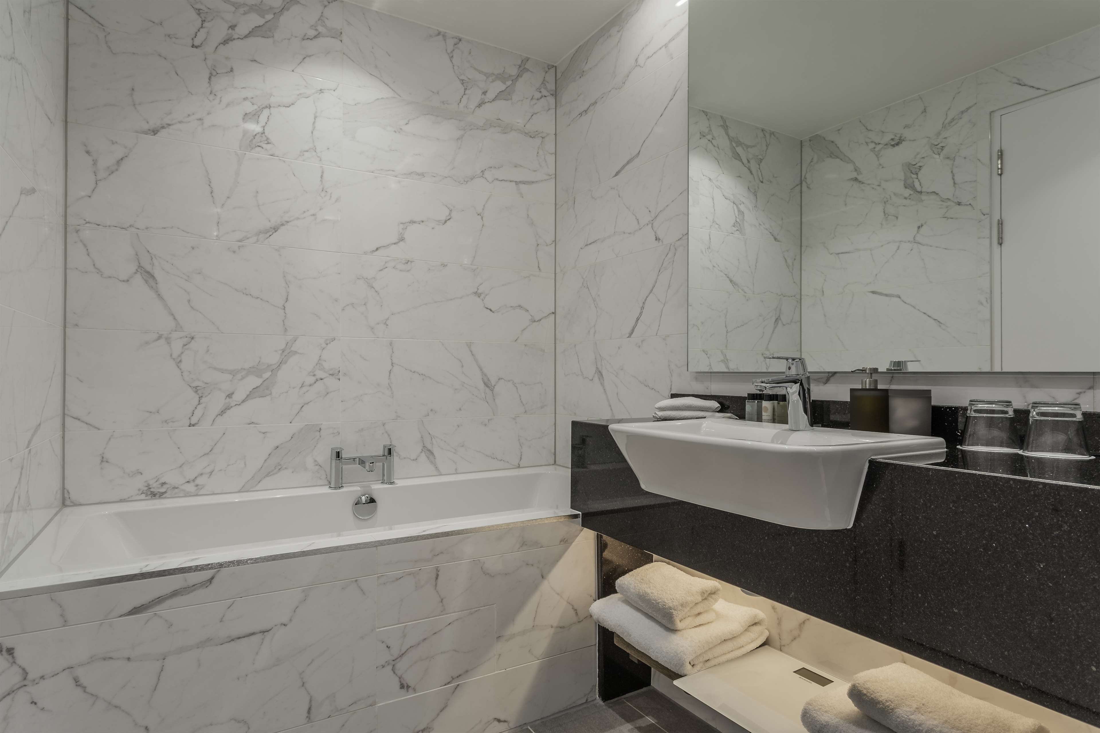 A modern bathroom with a marble wall, a freestanding bathtub, a vanity with a sink, and a mirror.
