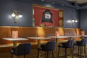 Um restaurante com cabines e mesas altas, parede vermelha com um relógio e iluminação embutida.