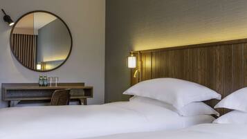 A hotel room with a large round mirror, a wooden headboard, and a bedside table with two bottles and glasses.