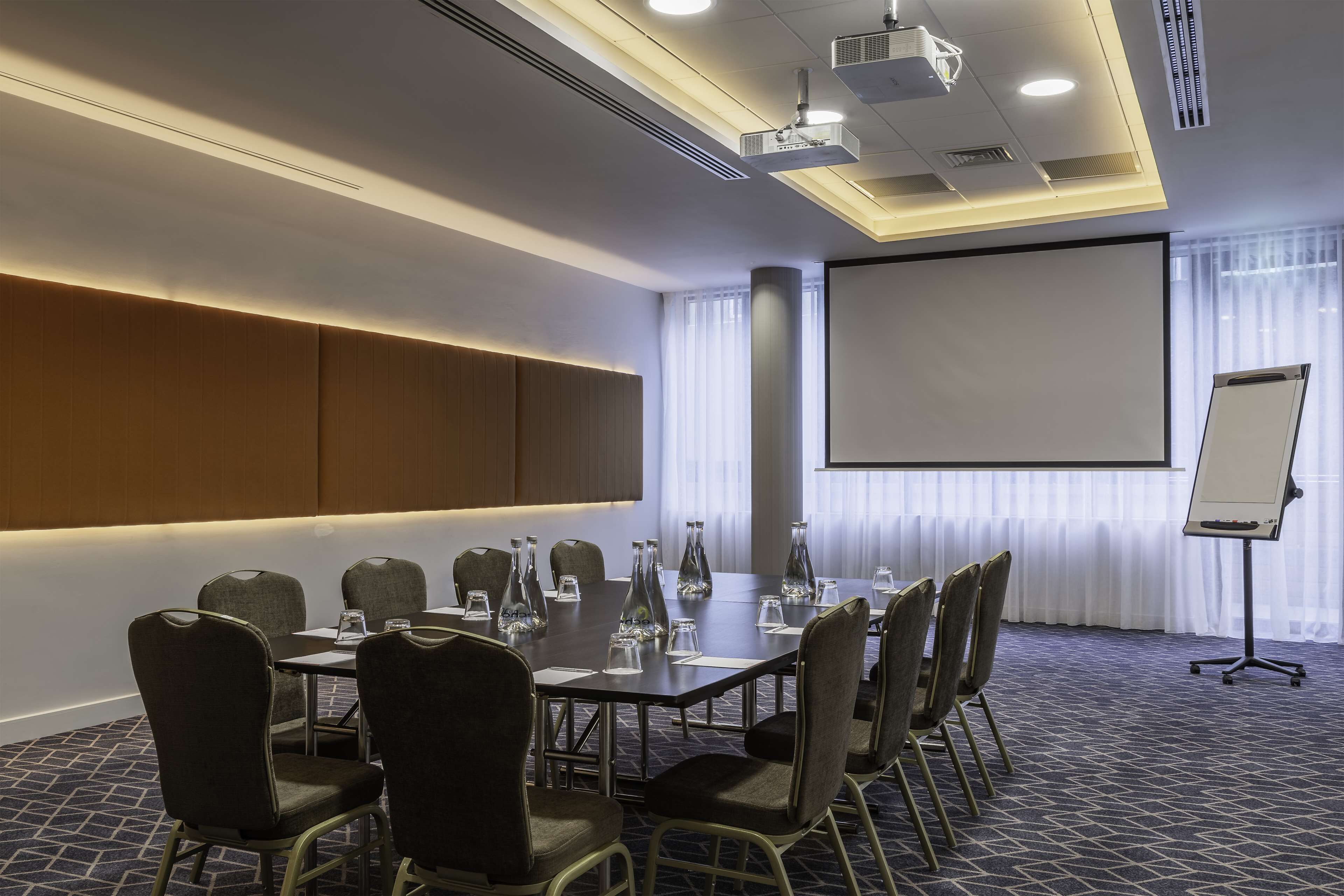 A conference room with a large table, chairs, a projector screen, and a whiteboard.