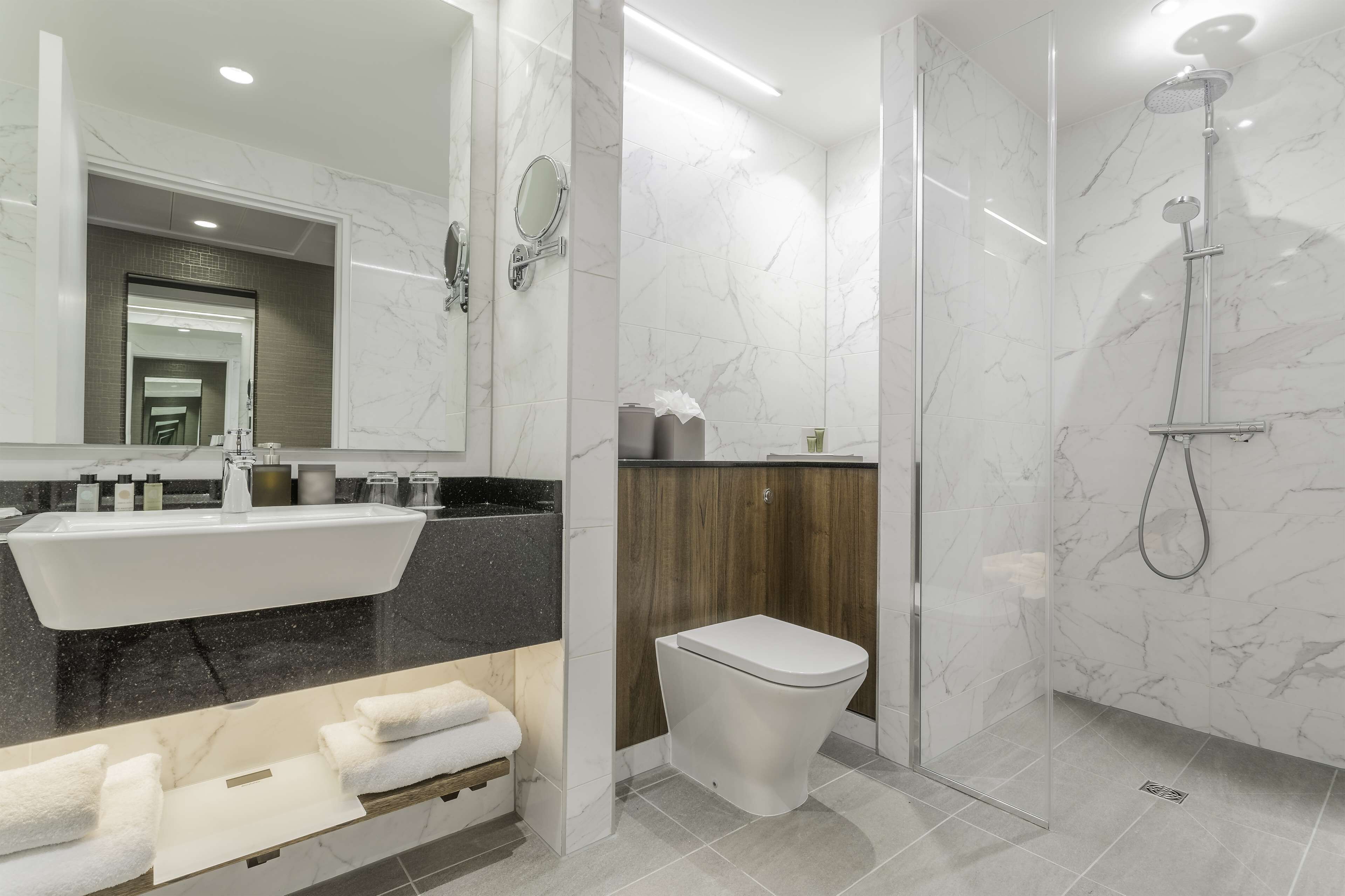 A modern bathroom with a large mirror, a sink, a toilet, and a shower.