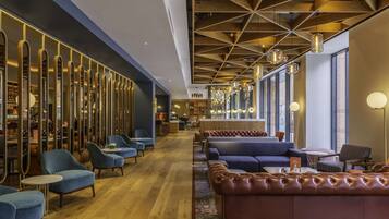 Un moderno vestíbulo de hotel con zonas de estar, un bar y una cocina al fondo.