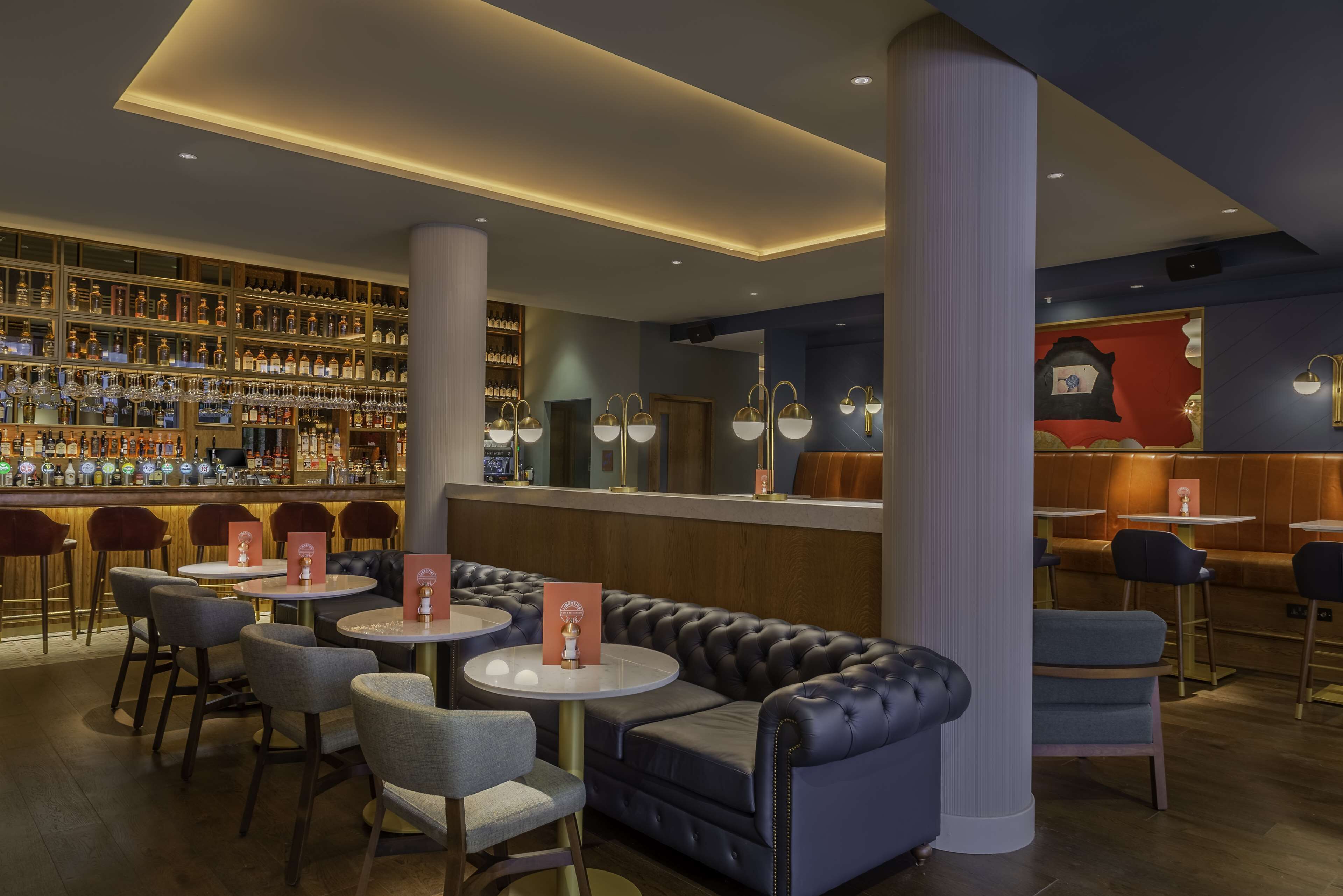 A bar area with multiple seating options, including round tables and a sofa, and a well-stocked liquor display.