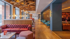 Een moderne hotel lobby met een rode leren bank, houten plafond en een blauwe zithoek.