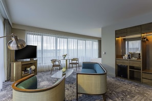 A hotel room with a flat-screen TV, a sofa, a coffee table, and a dining area with chairs.