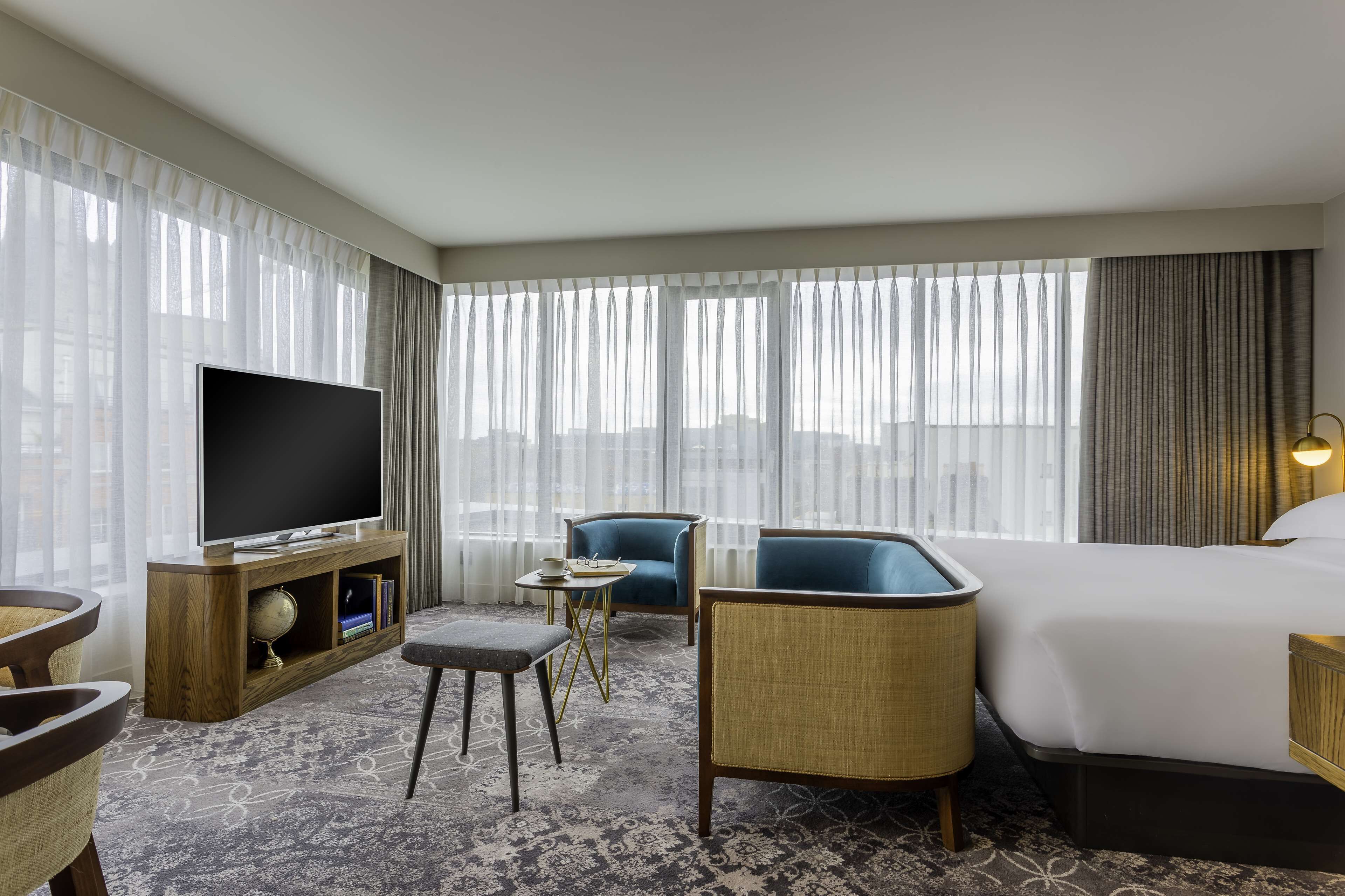 A hotel room with a large bed, a television on a wooden stand, a small table with a globe, two armchairs, and a sofa.