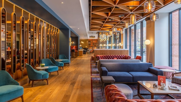 Een moderne hotellobby met zithoeken, een bar en uitzicht op de stad door grote ramen.